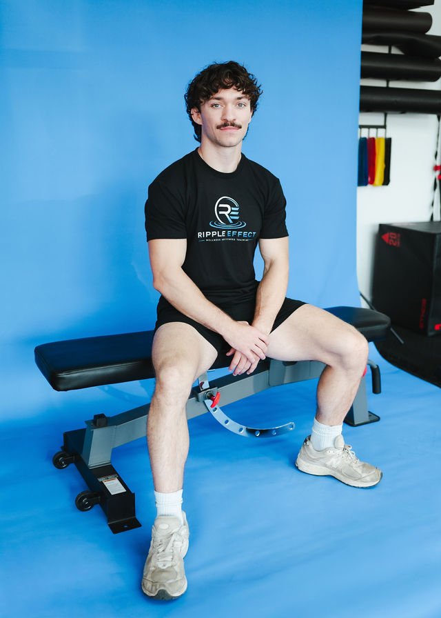 Chase, founder of Ripple Effect, seated on a training bench in his black Ripple Effect shirt